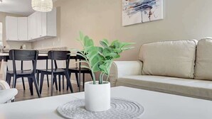 Ein modernes Wohnzimmer mit einem weißen Sofa, einem Essbereich mit schwarzen Stühlen und einem weißen Tisch mit einem Blumentopf.
