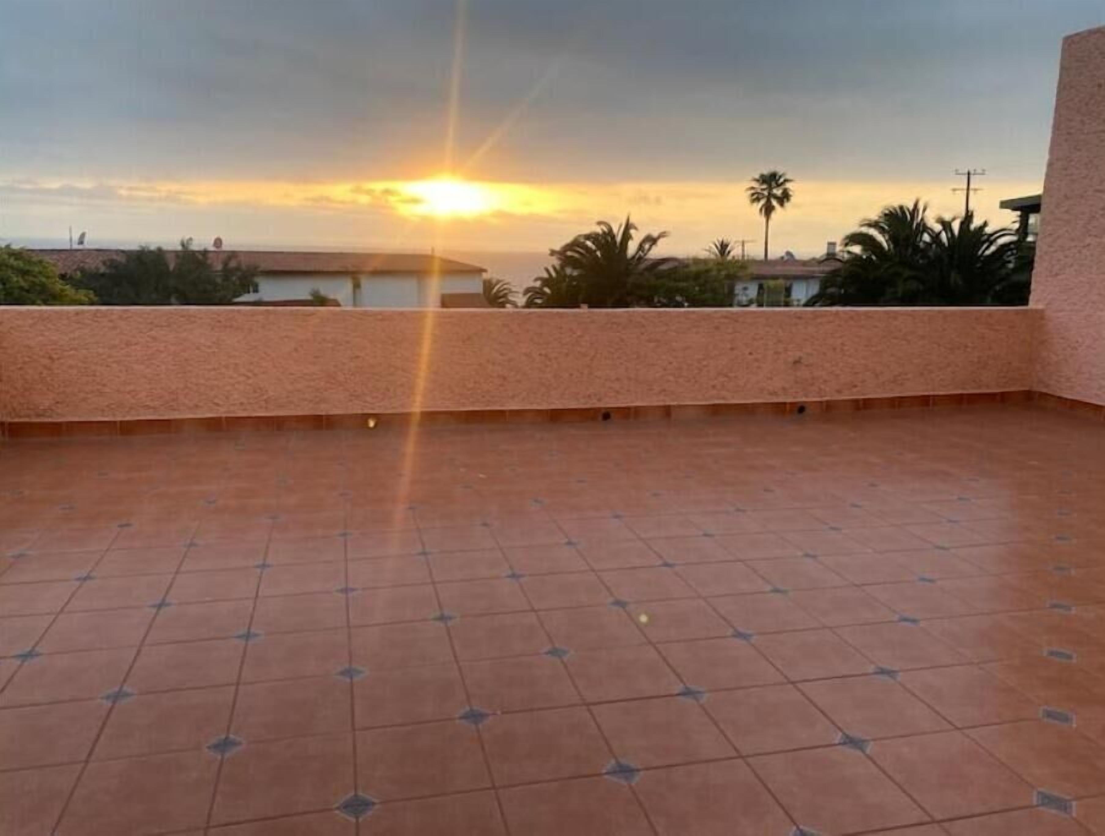 Une terrasse sur le toit offrant une vue sur le coucher du soleil, avec un sol carrelé et un petit muret.