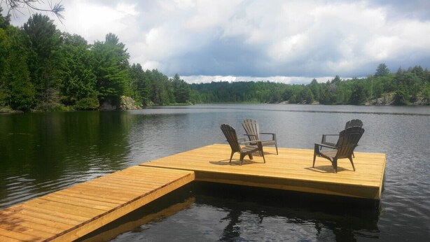 Une jetée en bois s’avançant dans un lac, avec deux chaises Adirondack qui y sont placées.