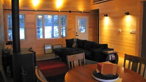 Un intérieur de chalet chaleureux, avec un revêtement mural en bois, une cheminée, un canapé, une table à manger et un escalier menant à un niveau supérieur.