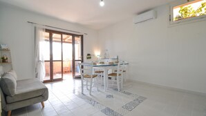Ein geräumiger Wohnbereich mit einer Couch, einem Esstisch für vier Personen und einer Glastür, die auf eine Terrasse im Freien führt.