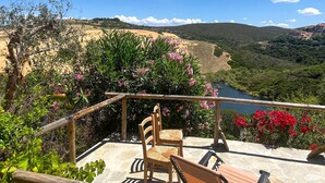 Eine Terrasse mit Steinbelag, Holzstühlen und einem Tisch mit Blick auf einen Fluss und eine hügelige Landschaft.