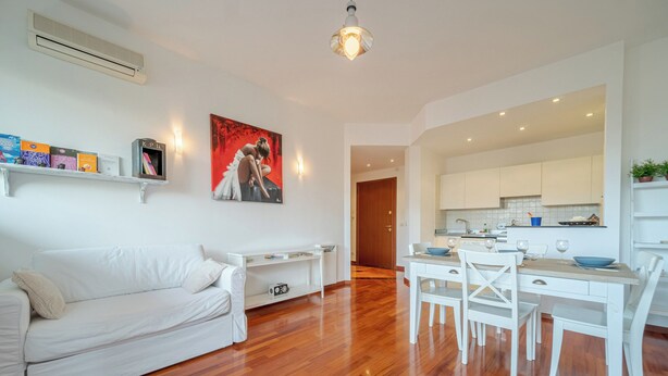 A modern living room with a white sofa, a dining table with chairs, and a kitchen area visible through an open doorway. - Genoa Getaway! Sturla Comfy Flat X2 Free Parking (Genoa)