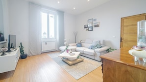 A modern living room with a white sofa, a coffee table, a wooden cabinet, and a large window. - Bright Apartment A Few Steps From Via Garibaldi (Genoa)
