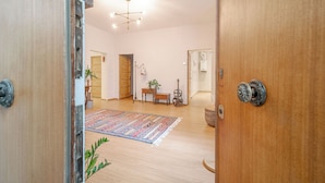 A room with a wooden floor, a patterned rug, a wooden door, a ceiling light fixture, and a small table with a plant. - Bright Apartment A Few Steps From Via Garibaldi (Genoa)