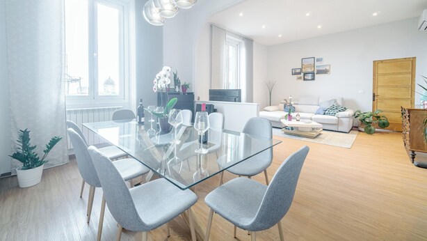 A modern living room with a glass dining table, grey chairs, a white sofa, and a wooden cabinet. - Bright Apartment A Few Steps From Via Garibaldi (Genoa)