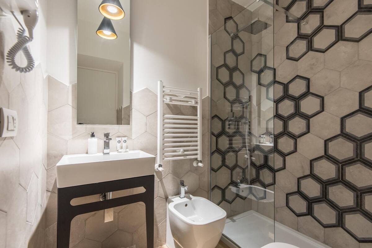 Une salle de bain moderne avec un lavabo blanc, un socle noir et une douche en verre avec des carreaux hexagonaux.