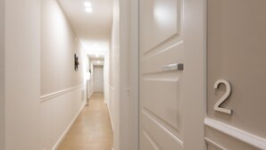 A hallway with a wooden floor and white walls, leading to a door marked with the number 2. - Five Boutique Rooms (Naples)