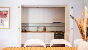A modern kitchen with white cabinets, a wooden table, and two white chairs. - Pimpinnacolo (Monte Argentario)