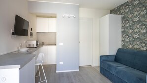 Eine moderne Küche mit Flachbildfernseher, Mikrowelle und einem Weinglas auf der Arbeitsfläche. Ein blaues Sofa und eine Tür zu einem weiteren Raum sind ebenfalls vorhanden.