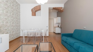 Ein modernes Wohnzimmer mit einem blauen Sofa, einem Esstisch mit Stühlen und einer durch einen Bogen sichtbaren Küchenzeile.
