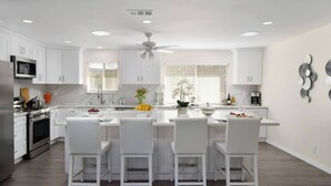 Una cucina moderna con mobili bianchi, un'isola centrale con sedute, forno integrato e ventilatore a soffitto.