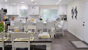 Una cucina moderna con mobili bianchi, un'area pranzo con tavolo apparecchiato per quattro persone e una ventola a soffitto.