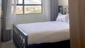 Una camera d'albergo con un letto grande, una finestra con tende e vista sugli edifici.