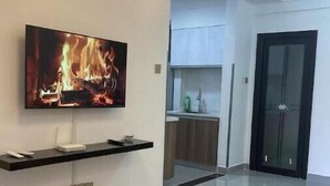 Un soggiorno moderno con una televisione a schermo piatto montata a parete, un tavolino in legno e una cucina visibile attraverso una porta aperta.