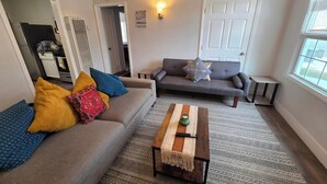 Un salon avec un canapé gris, des coussins colorés, une table basse en bois et un tapis à motifs.