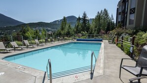 Une piscine avec des chaises longues, un panneau indiquant qu’il est interdit de plonger, et une vue sur les montagnes.