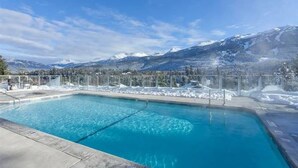 Une piscine à l’eau d’un bleu cristallin, entourée d’une clôture métallique, et offrant une vue sur des montagnes enneigées sous un ciel dégagé.