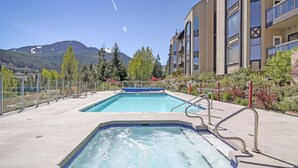 Un espace piscine doté de deux bains à remous, entouré d’un bâtiment avec des balcons et une montagne en arrière-plan.