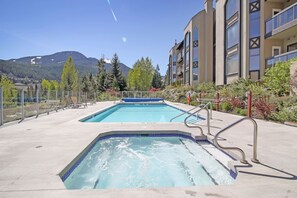 Zona de piscina con dos jacuzzis, rodeada por un edificio con balcones y una montaña al fondo.