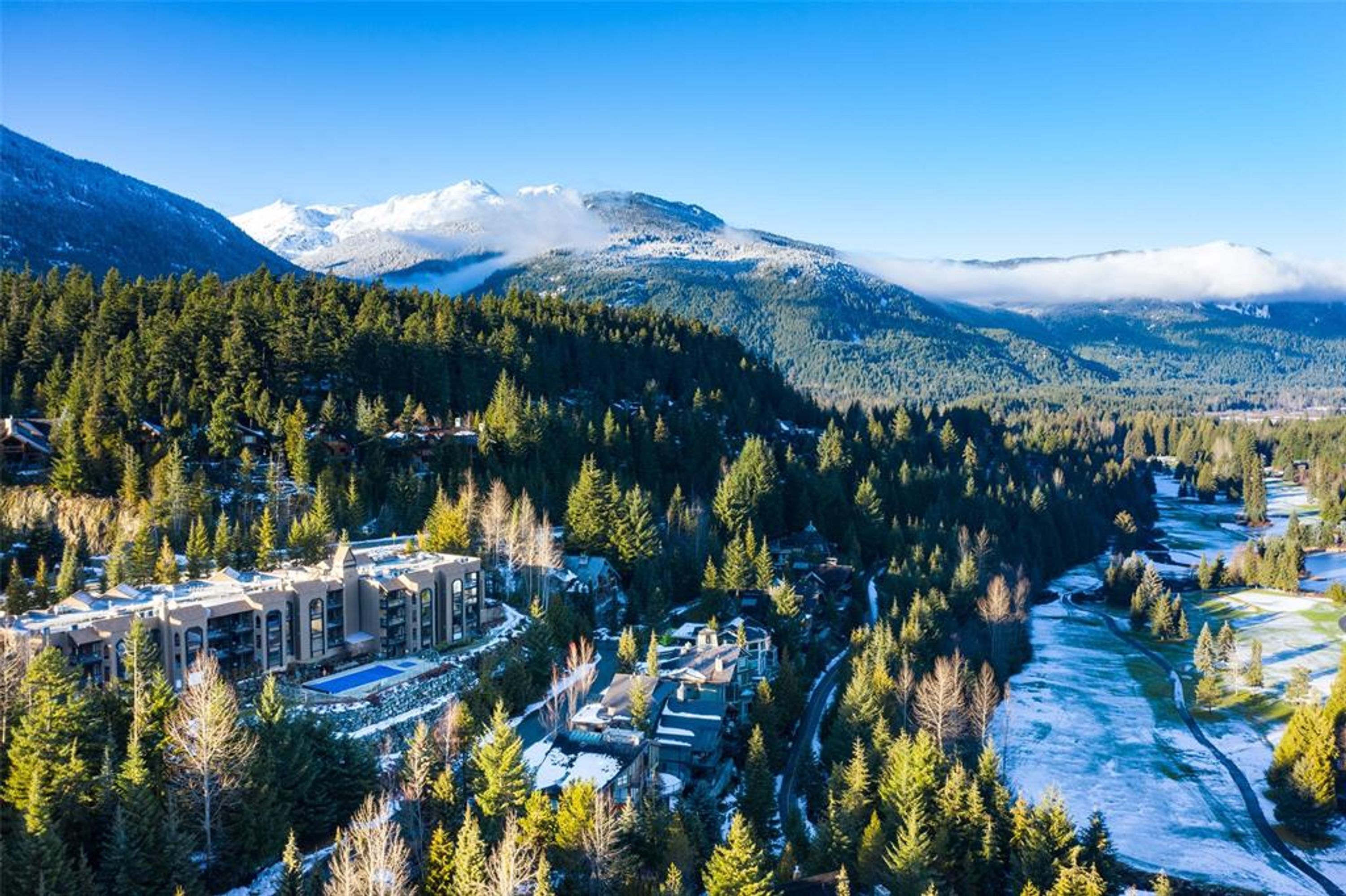Paisaje montañoso con un río, un bosque denso y un conjunto de edificios con varias construcciones.