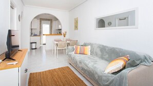 Una sala de estar moderna con un sofá gris, un escritorio de madera, un televisor y un ventilador de techo.