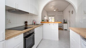 Una cocina moderna con armarios blancos, encimera de madera y un arco que conduce a un comedor.