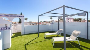 Terraza en la azotea con césped artificial, sillones blancos y una estructura de pérgola.