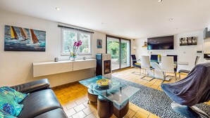 A modern living room with a sofa, a glass coffee table, and a TV. There is a window with a view of greenery outside.