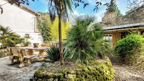A rustic outdoor seating area with stone tables and chairs, surrounded by lush greenery and a moss-covered rock feature.