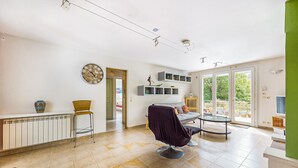 A spacious living room with a large window, a dining area, and a seating area with a chair and a table.