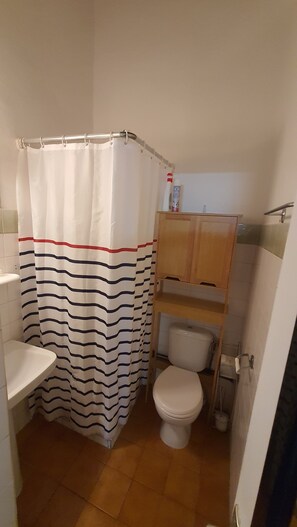 A bathroom with a striped shower curtain, a toilet, a sink, and a wooden cabinet.