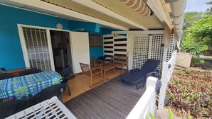 A covered patio area with a table and chairs, a wooden bench, and a lounge chair. - Bungalow Style Studio vue Mer, Accès Direct Plage Véhicule de Location Possible (La Trinité)