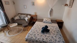 A room with a bed, a sofa, a small table, and a chair. - Bungalow Style Studio vue Mer, Accès Direct Plage Véhicule de Location Possible (La Trinité)
