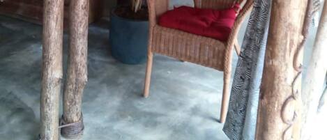 Una habitación rústica con una mesa de madera, una planta en maceta, una silla de mimbre y un muro con adornos circulares.