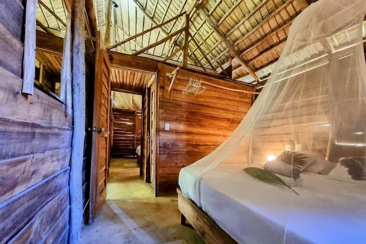 Une pièce rustique en bois, avec un lit, une porte donnant sur une autre pièce et un toit de chaume.