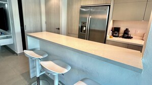 A modern kitchen with a central island, bar stools, a built-in refrigerator, and a coffee machine. - NEW 3/2 POOLFRONT. FULL BACKUP GENERATOR, 2 POOLS, NEAR BEACH, GYM, 2 PARKINGS. (Carolina)