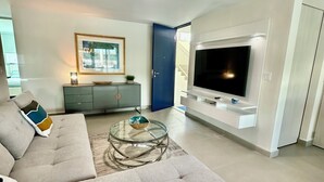 A modern living room with a large grey sectional sofa, a glass coffee table, a flat-screen TV mounted on the wall, and a grey cabinet with a framed picture above it. - NEW 3/2 POOLFRONT. FULL BACKUP GENERATOR, 2 POOLS, NEAR BEACH, GYM, 2 PARKINGS. (Carolina)