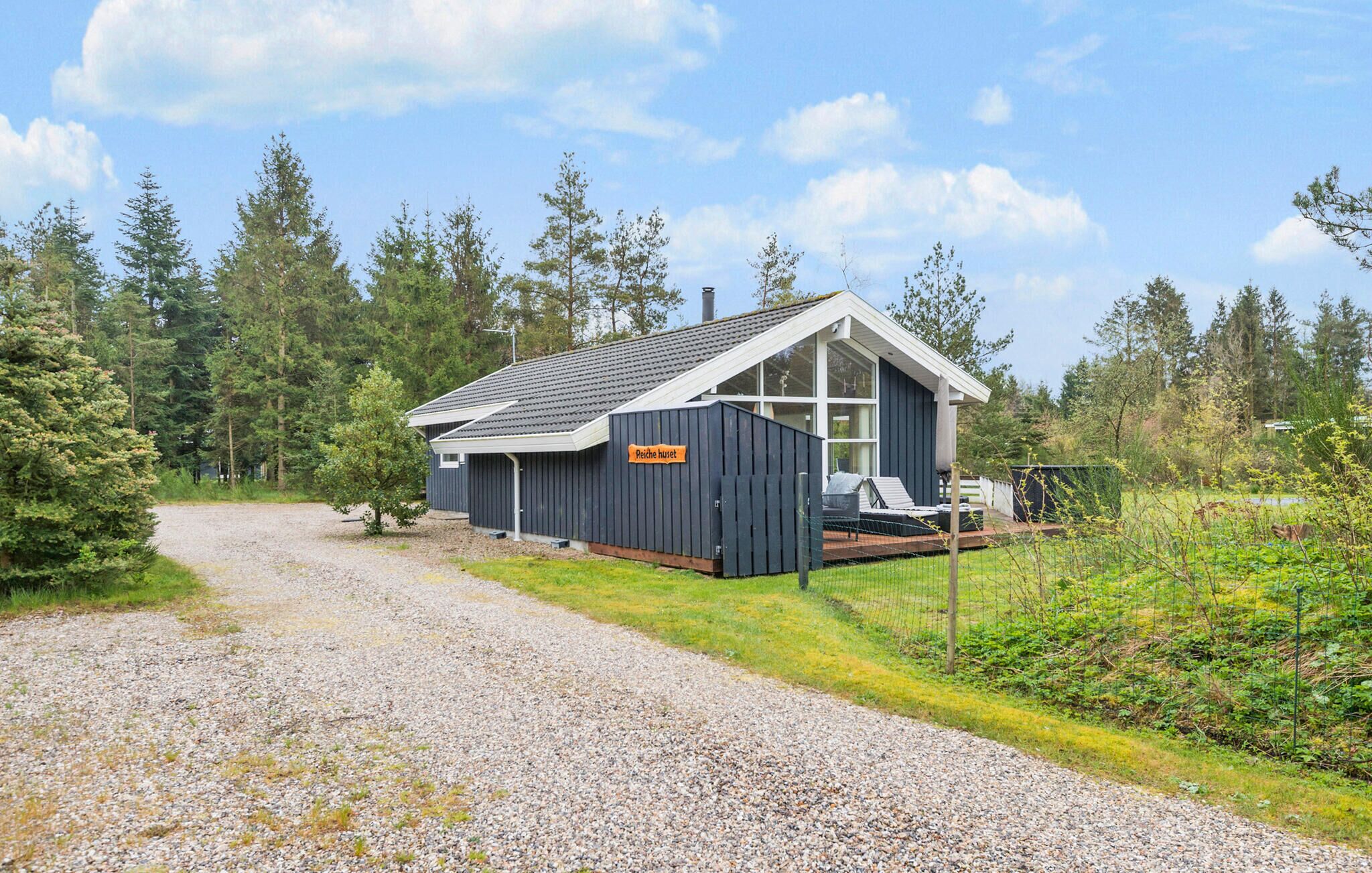 Een klein vakantiehuisje met een grindpad dat erheen leidt, omringd door bomen en een gazon.