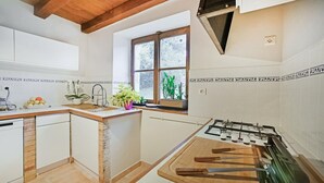 Een keuken met witte kasten, een houten aanrecht, een gasfornuis en een raam met planten.