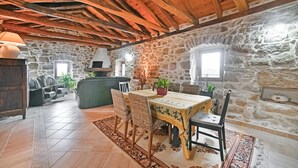 Een rustiek stenen interieur met een houten plafond, een stenen openhaard, een eettafel met stoelen en een leren bank.