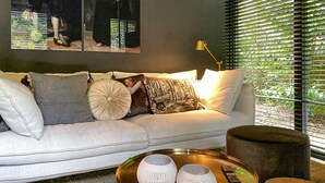 A modern living room with a white sofa, patterned cushions, a coffee table with two white vases, and a window with blinds. - Nice home in Rheezerveen with sauna (Rheezerveen)