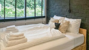 A neatly made bed with white linens and folded towels, a wooden headboard, and a window with blinds. - Nice home in Rheezerveen with sauna (Rheezerveen)