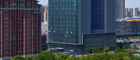 A modern high-rise hotel with a glass facade, surrounded by a park with playgrounds and a running track.