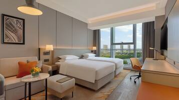 A modern hotel room with a large bed, a desk, a sofa, and a view of the city.