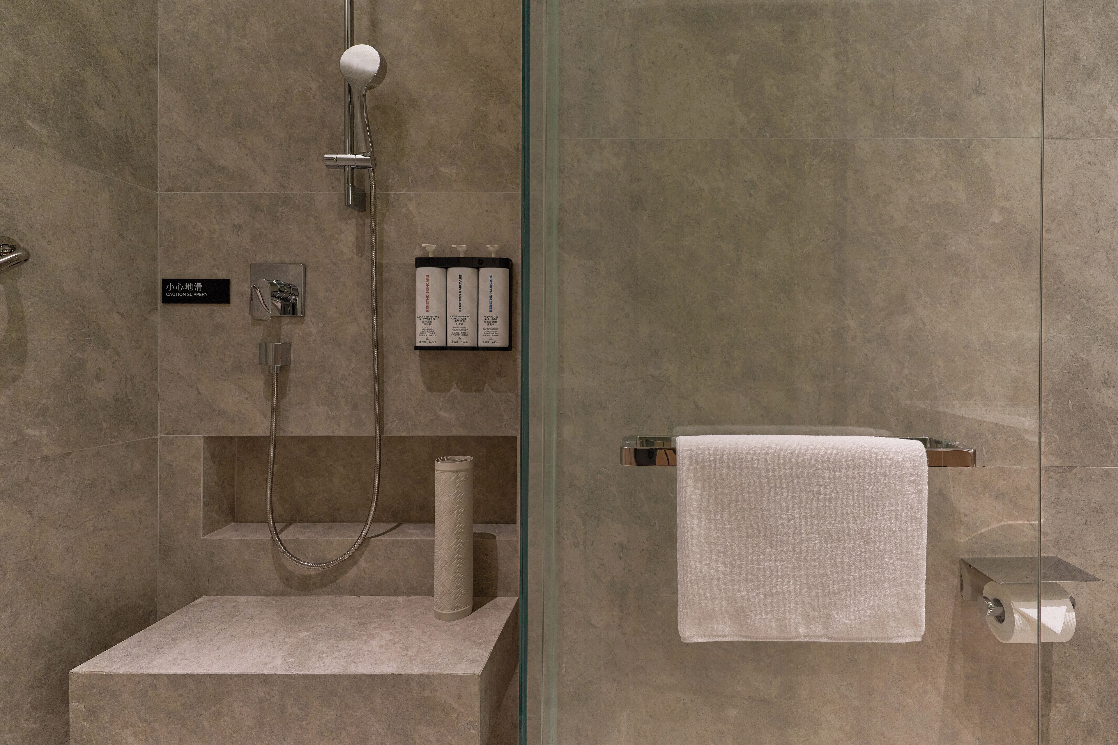 Een moderne badkamer met een douche met glazen wand, een handdoekhouder en een toiletrolhouder.