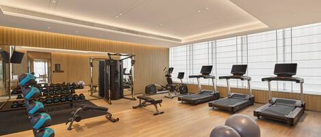 A modern gym with treadmills, elliptical machines, free weights, and exercise balls.