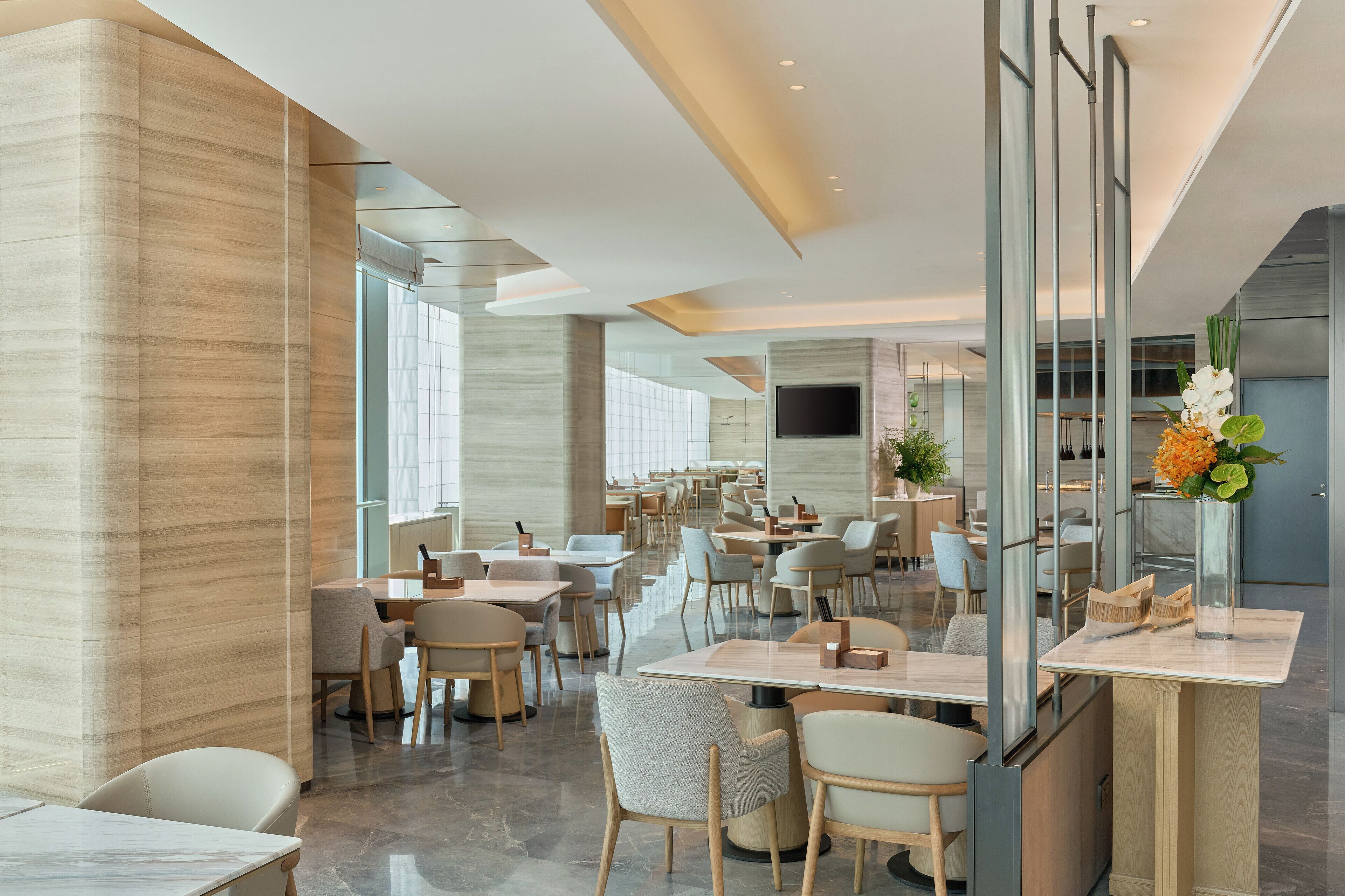 A modern restaurant with a spacious layout, large windows, and a flat-screen TV mounted on the wall.