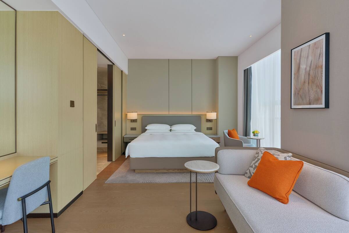 A modern hotel room with a bed, a sofa, a desk, and a small table.