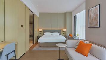 Quarto de hotel moderno com cama, sofá, escrivaninha e uma mesinha.